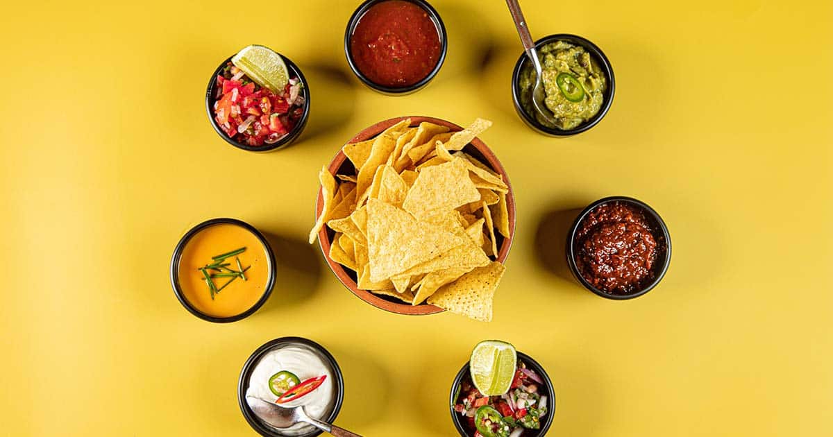 Mexican cuisine on a yellow background including tortilla chips and various dips